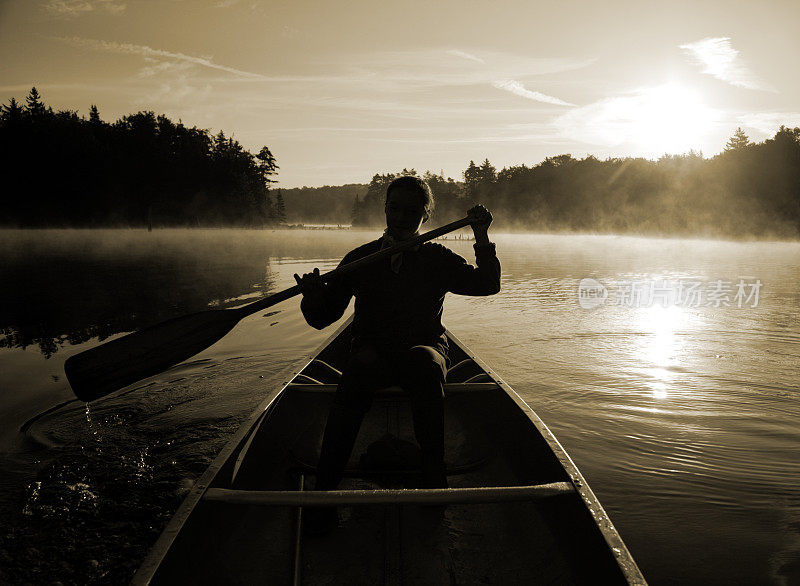 户外女孩划着小舟在雾蒙蒙的湖面上背光日出