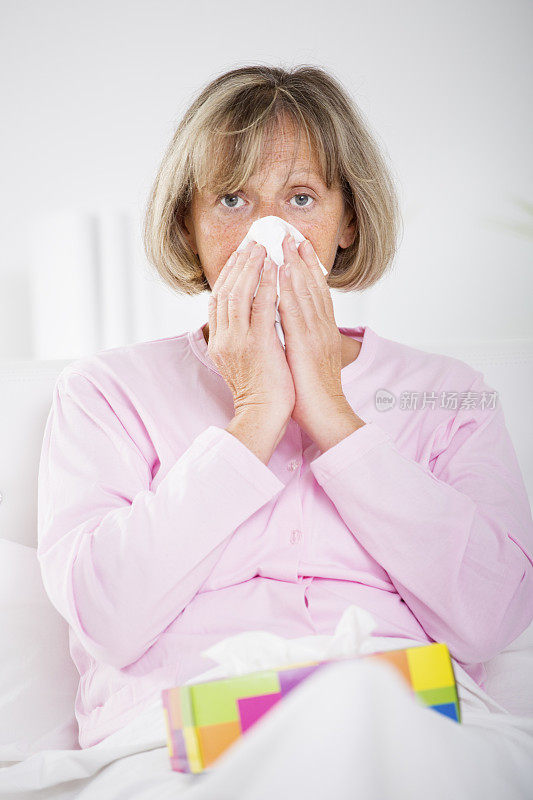 正在擤鼻涕的生病老妇人。