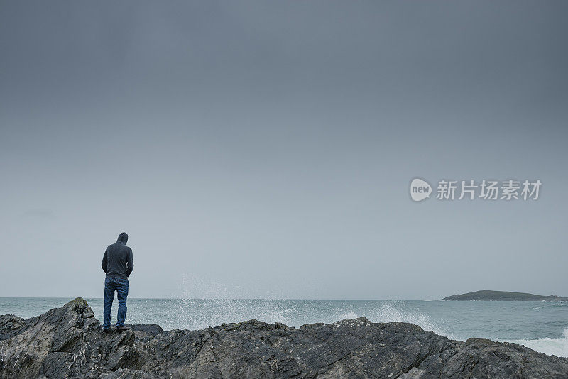 在阴沉的天气里，人们站在海岸线上的岩石上。