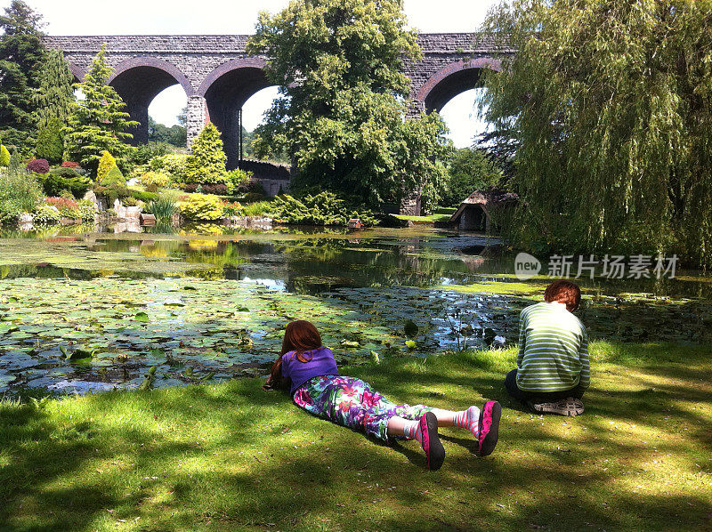 孩子们在园林池塘边放松的画面