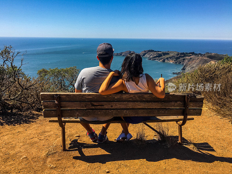 一对年轻夫妇坐在长椅上欣赏美妙的海景