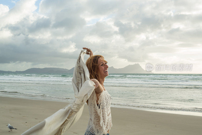 一个白人妇女在风中拿着毯子在沙滩上的肖像