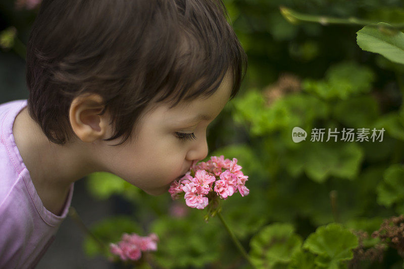 小女孩的肖像闻花对树区域和花时间在花园里