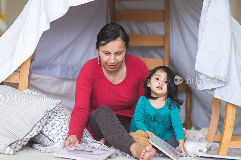美国土著妈妈和她的女儿在客厅里临时搭建的堡垒下读书