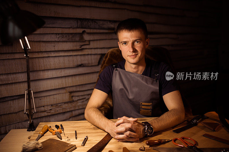 皮带在皮革车间的工作过程。男人在木桌上牵着手。制作工具的背景。旧制革厂的皮匠。靠近男人的手臂。联锁的手指