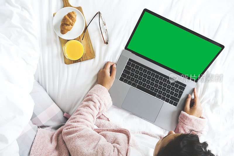 年轻女子在床上使用绿色屏幕的笔记本电脑。