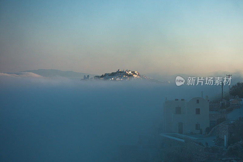 在阳光明媚的日出时分，位于圣托里尼岛伊梅洛维格利村的破火山口悬崖上方的雾