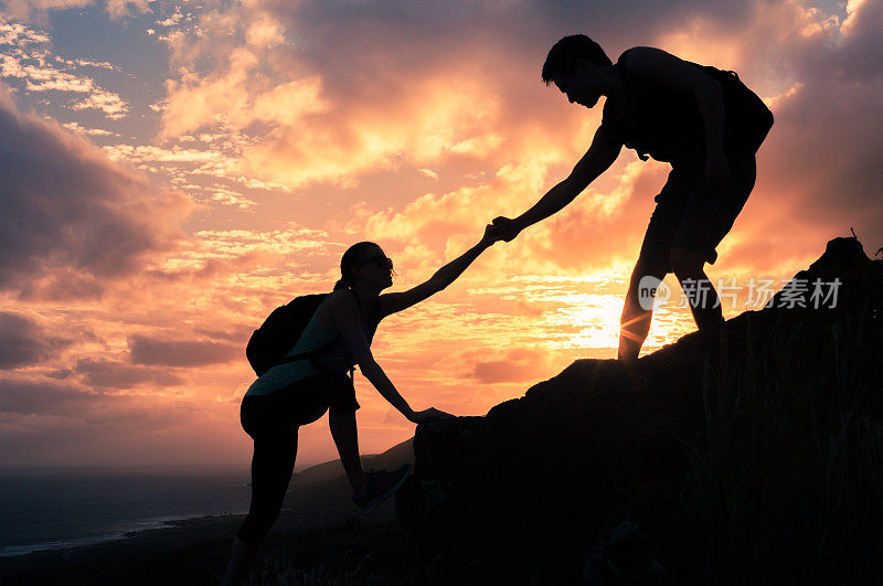 一男一女徒步者正在攀登悬崖，其中一人伸出援手