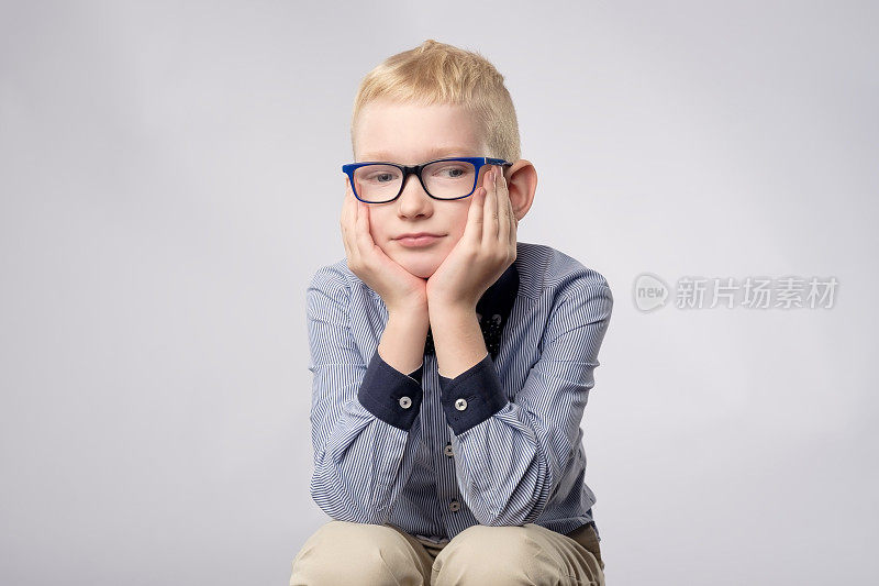 白人金发男孩的肖像戴着眼镜看着无聊的面部表情相机在白色的背景。