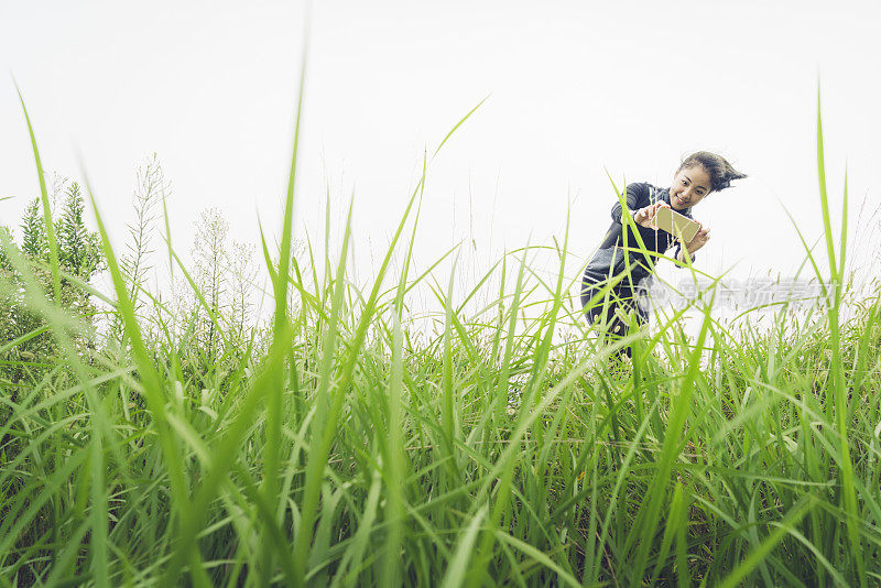 疲惫的女孩用智能手机在草地上拍摄美丽的风景