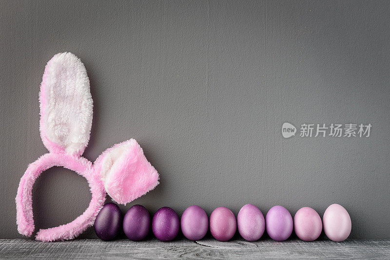 复活节彩蛋在一个时尚的颜色，在一个灰色的木制背景与一个女环与复活节兔子耳朵