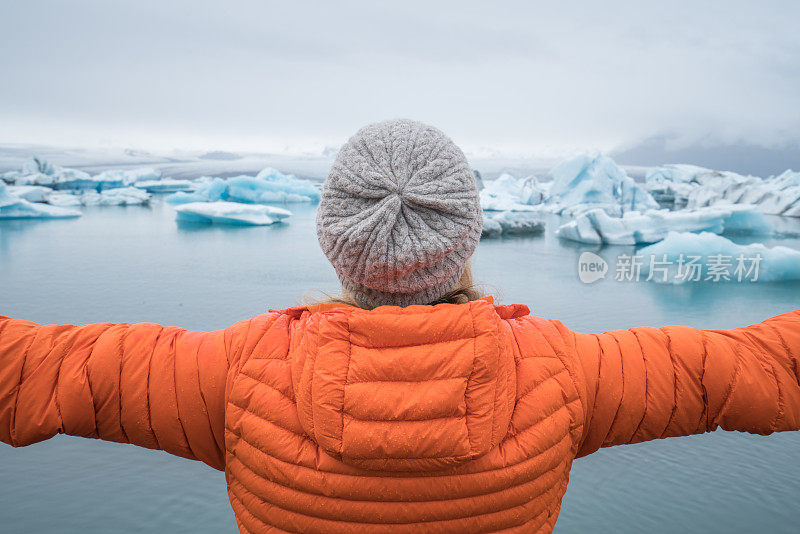 年轻女子在冰岛的冰川泻湖伸出双臂，表达自由和热爱自然的概念