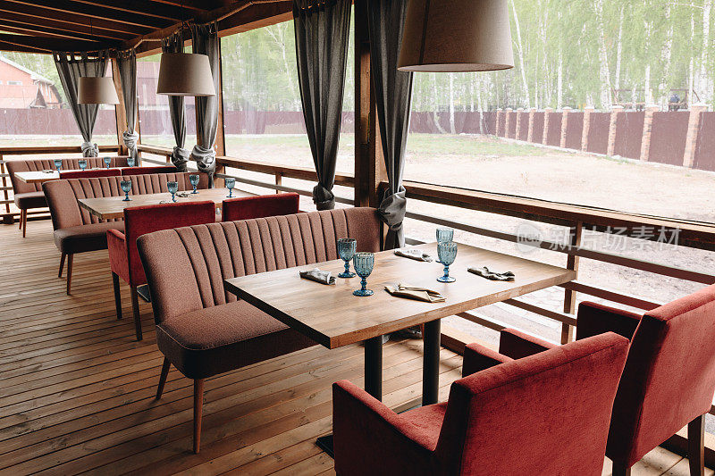 乡村餐厅夏日露台:木桌与摆设，优雅的沙发和椅子，悬挂古典灯具