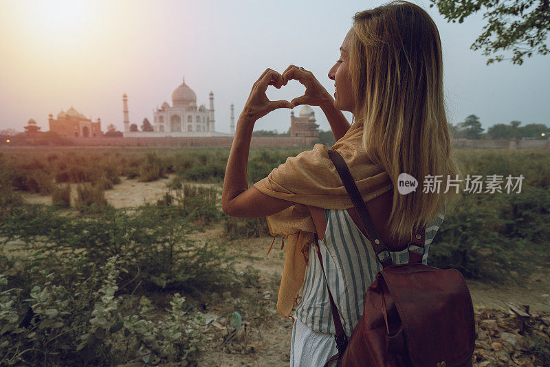 年轻女子喜欢著名的泰姬陵在日落做心形的手指框架