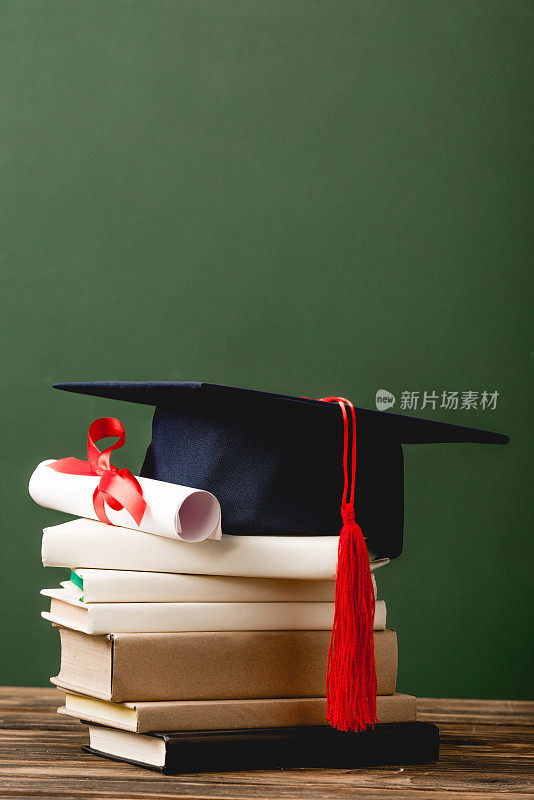 书籍、学位帽和毕业证书在木质表面隔离在绿色上