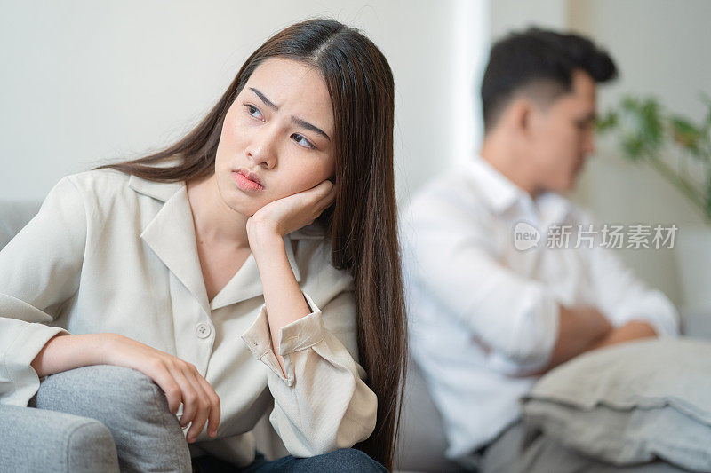 年轻夫妇在家里吵架。悲伤的年轻亚洲女人和男朋友坐在沙发上。夫妻关系问题和沟通问题的概念