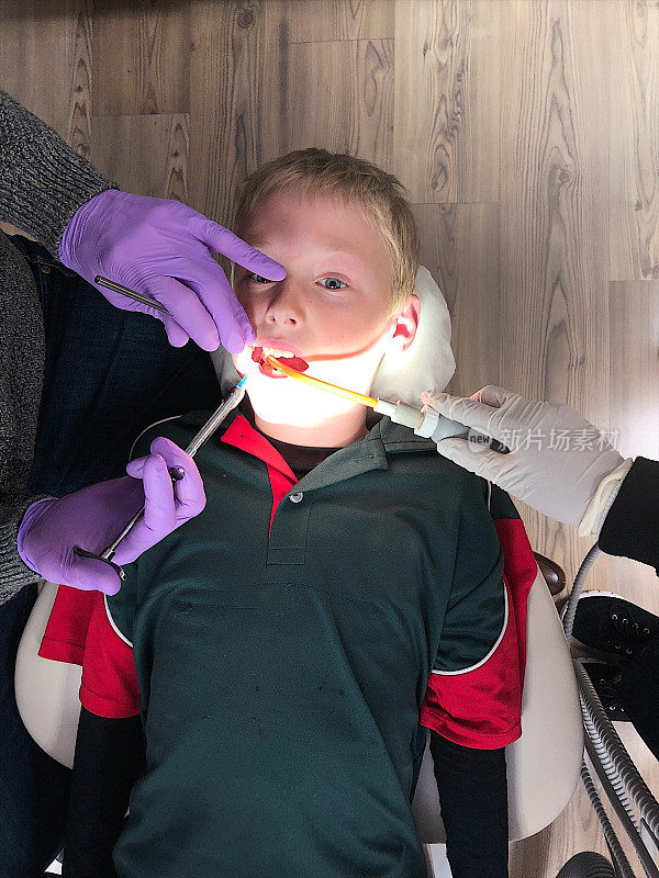 牙医使用注射器局部麻醉剂给一个男孩拔牙