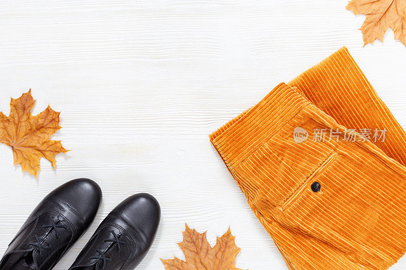 明亮的秋天平躺与黑色的靴子和时尚的橙色灯芯绒裤子在白色的木材背景与拷贝空间。女人舒服的衣服。前视图。