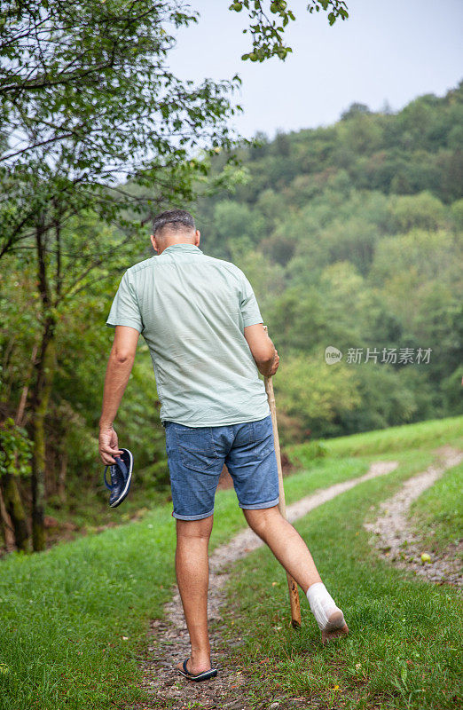 一个成年男子扭伤了脚踝，走在乡间小路上