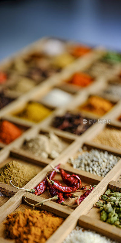 各种彩色的，有机的，干燥的，充满活力的印度食物香料在一个乡村木隔间托盘与蓝色的背景。