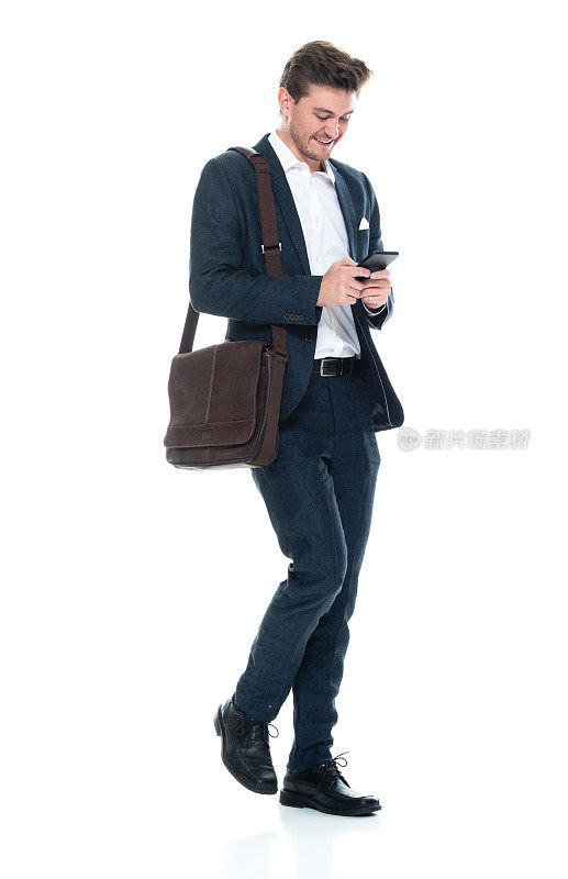 白人男性经理走在白色背景前，戴着邮差包，拿着包，使用手机