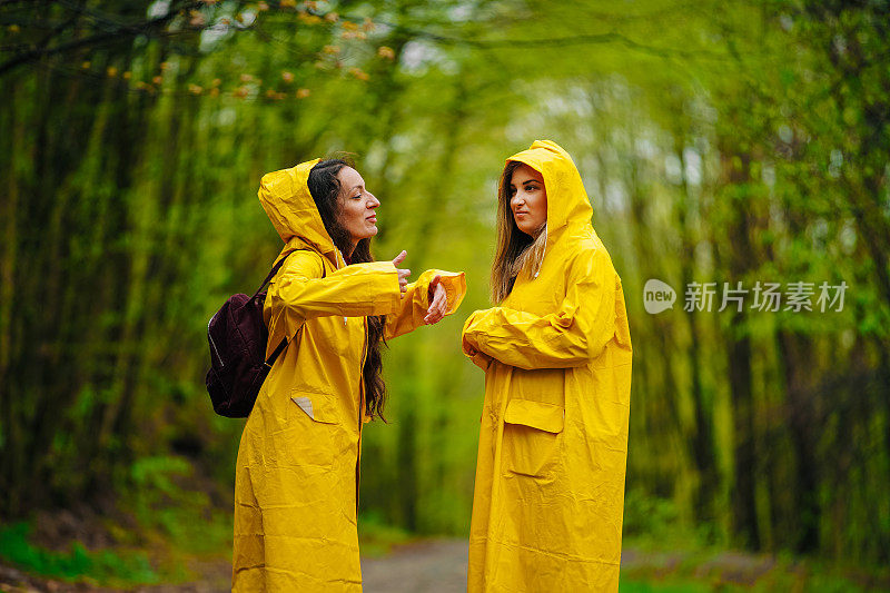 两个穿着雨衣的女性朋友在雾霾的森林里在雨中奔跑