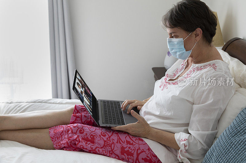 妇女生病在床上戴着口罩用笔记本电脑群视频聊天