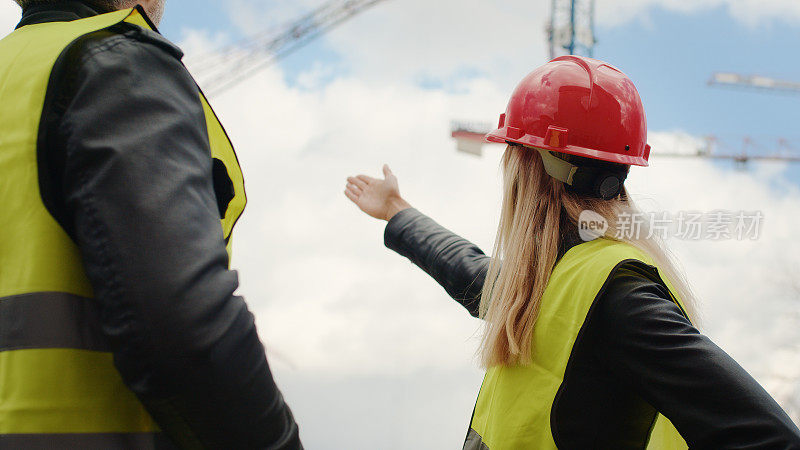 女建筑工程师监督建筑工地。指向起重机