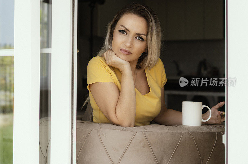 年轻漂亮的女人坐在沙发上喝着咖啡在家