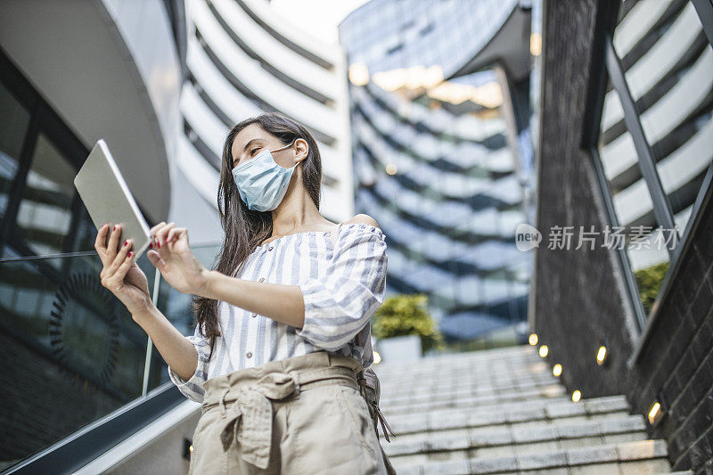 美丽的女人站在城市街道上使用数字平板电脑，脸上戴着防护面具。病毒大流行和污染概念。