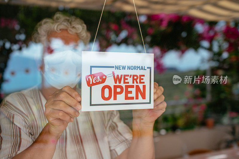 一名妇女戴着口罩，举着一个小商店的开放标志