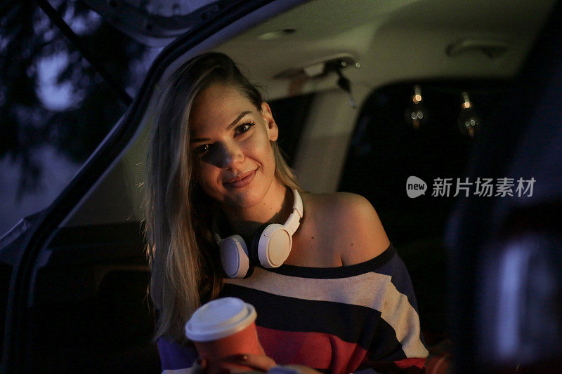 一个年轻漂亮的女人露营在车的后面，喝着热咖啡放松