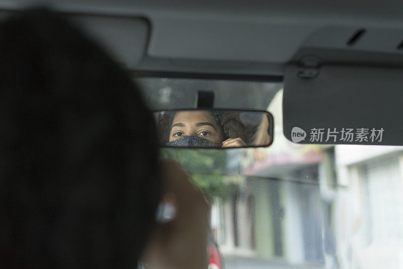 年轻女性司机在街道卫生检查站使用后视镜调整她的汽车上的面罩。Covid-19概念