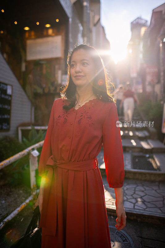 日落时分，年轻女子穿着红色裙子走在城市的台阶上