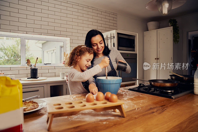 微笑的母亲帮助女儿在厨房搅拌鸡蛋和水面团