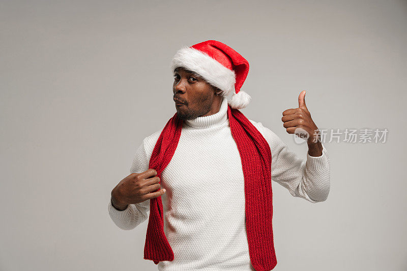 一个皮肤黝黑的年轻人，穿着羊毛衫，戴着圣诞帽，围着鲜红的围巾