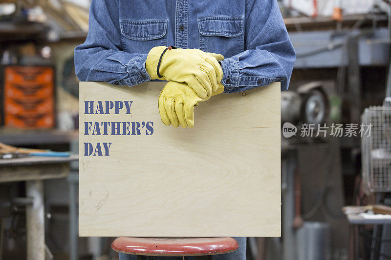 蓝领工人戴着工作手套举着“父亲节快乐”的牌子。