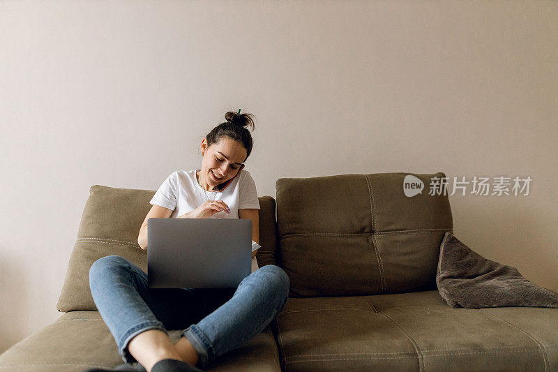 用笔记本电脑，笔记本电脑和智能手机在家工作的年轻女性