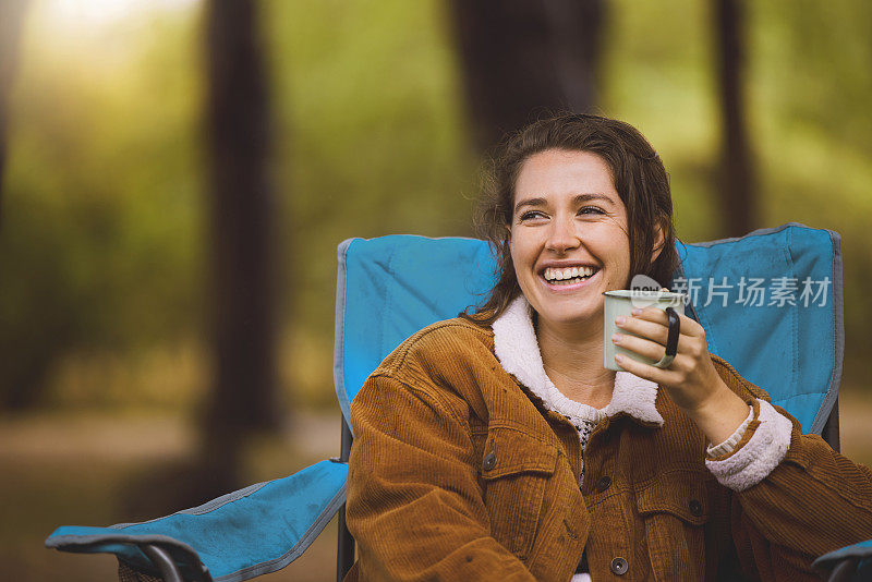 一个女人坐在户外露营的椅子上喝咖啡