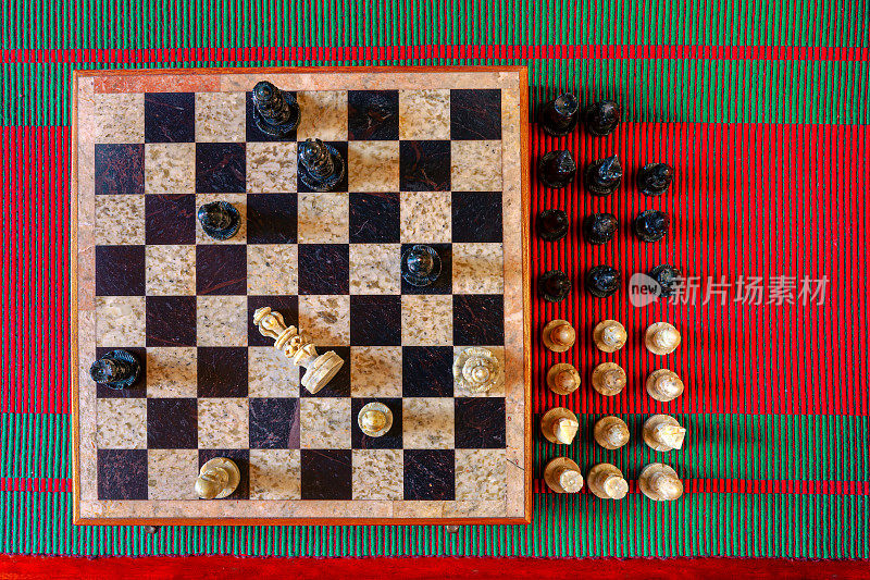 平放图像显示一个刚刚完成的象棋游戏;黑色赢了，被打败的国王倒下了。棋子由石头雕刻而成，棋盘上镶嵌着黑白有色的石头