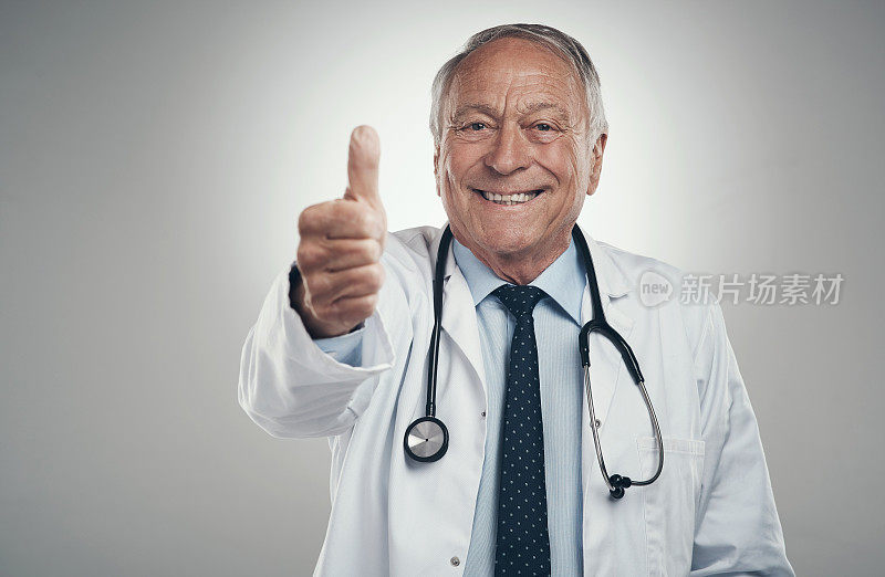 一名年长的男医生在摄影棚里对着灰色的背景竖起大拇指