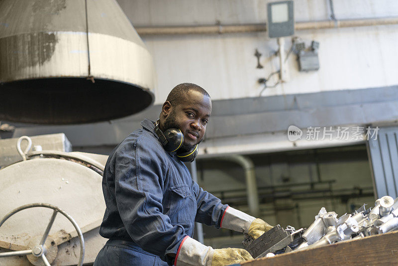 一名非裔美国工人在冶金工厂处理金属零件的肖像
