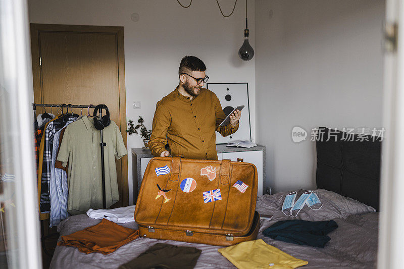 英俊的男人在酒店预订，准备旅行假期整齐地打包行李的衣服和配件