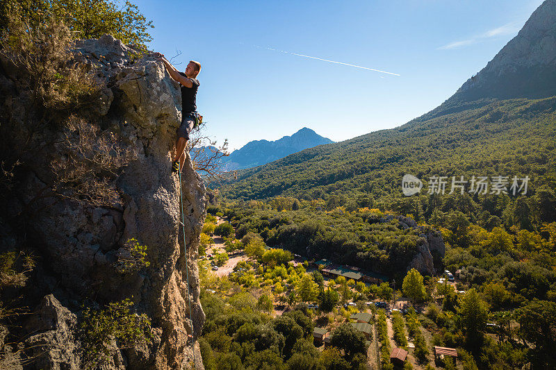 攀登者攀爬郁郁葱葱的山谷上陡峭的岩壁