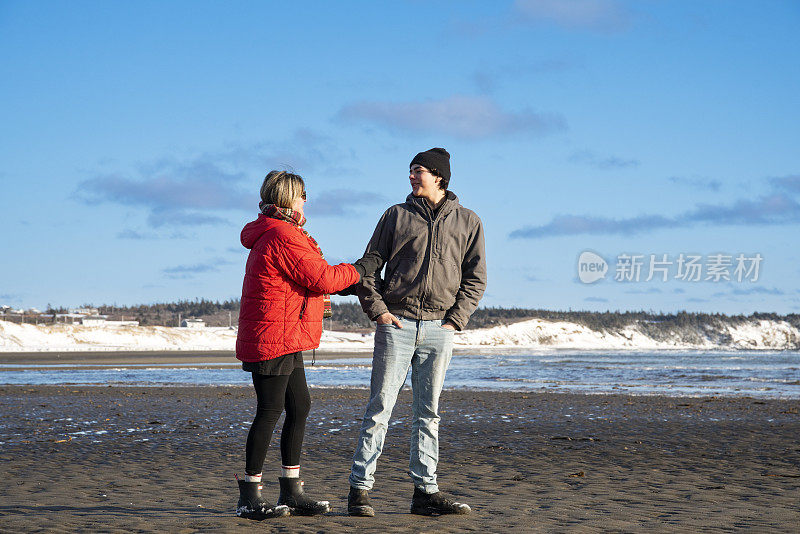 母亲和十几岁的儿子在冬天的沙滩上散步聊天