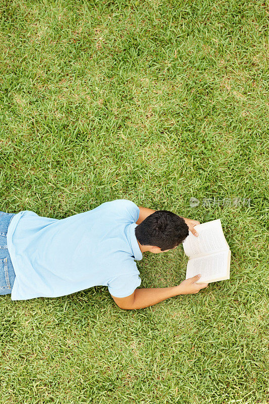 一个年轻人在草地上读着一本书