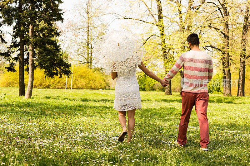 年轻夫妇在春天穿过公园的后视图