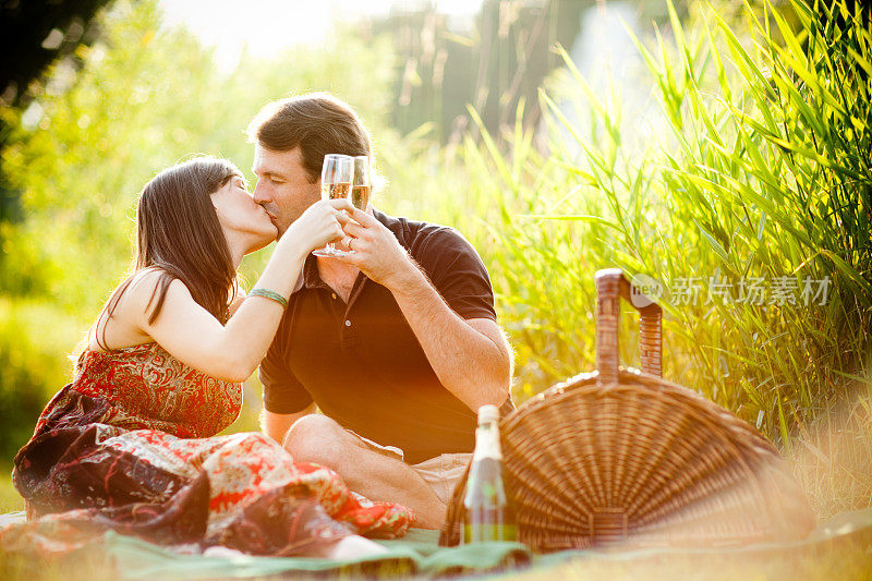 在浪漫的野餐中，情侣们一边亲吻一边用酒杯敬酒