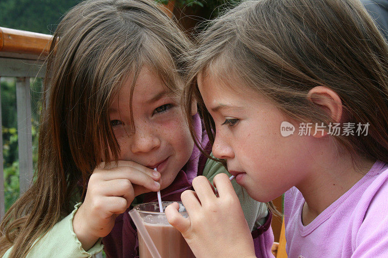 一对黑发的双胞胎女孩用吸管喝着可可