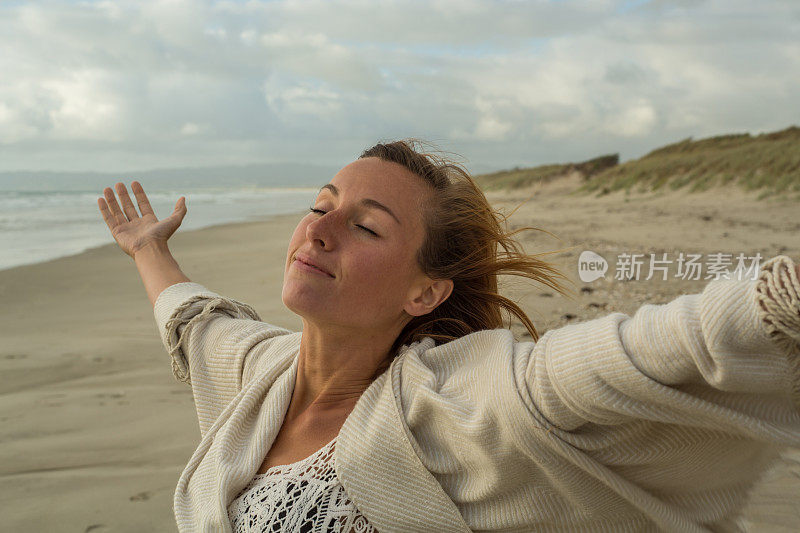 日落时分，快乐的年轻女子在海滩上张开双臂